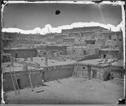 Multi-story adobe buildings and ladders at Zuni Pueblo in an 1873 photograph.
